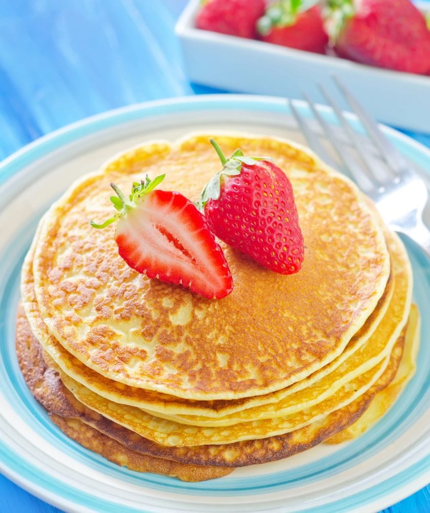 plate of cottage cheese pancakes with strawberry on top on blue background