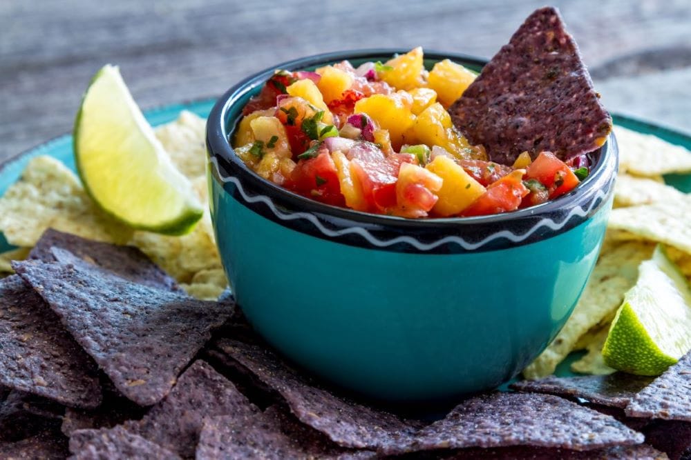 peach salsa in a blue bowl with a blue corn tortilla chip sticking in it